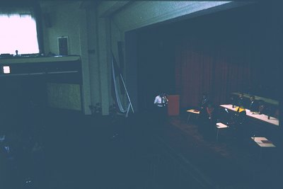 Vintage lecture hall with dim lighting, featuring a central podium and tiered seating. Stage equipment includes a microphone ...
