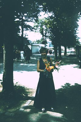 Vintage street portrait of a person in a long black dress holding a bouquet of flowers, likely tulips, with a blurred face. U...