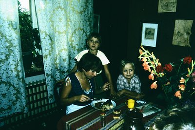 Family portrait in a mid-century interior, likely Eastern Europe, 1960s–1970s. Woman and child seated at a wooden table with ...