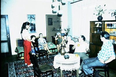 Vintage indoor gathering in a mid-century living room, featuring patterned carpet, wooden furniture, and framed art. A group ...