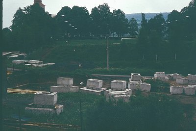 Pre-fabricated concrete bunkers arranged in a grid pattern on a sloped, overgrown field. Likely Cold War-era military infrast...