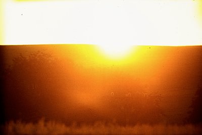Vintage film capture of a dramatic sunset over a body of water, likely coastal or lakeside. Warm golden light contrasts with ...