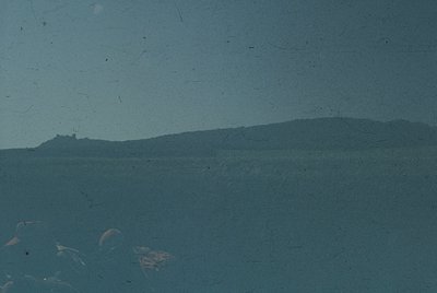 Vintage monochrome photo of a coastal landscape with faint ruins on a distant hill. Low-angle shot captures muted tones and g...