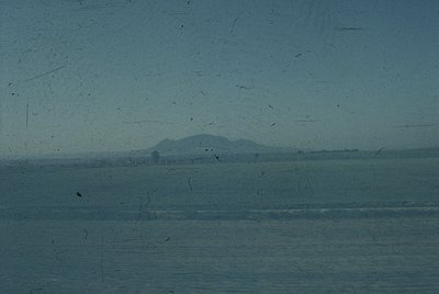 Vintage glass-paneled view of distant hilly terrain, likely from a train or ship. Distressed surface suggests aged archival m...