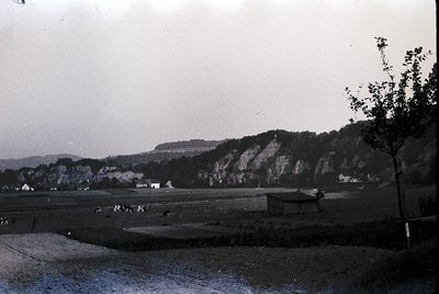 Black-and-white rural landscape featuring rocky cliffs, scattered farm buildings, and open fields. Mid-20th century agricultu...