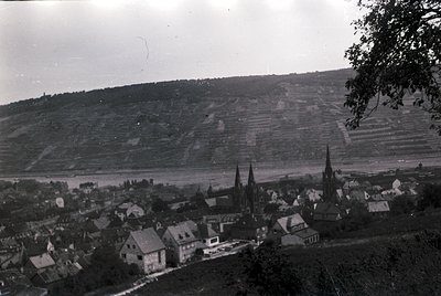 Black-and-white aerial view of a European village with Gothic spires and tiered agricultural terraces. Likely 1940s–1950s bas...