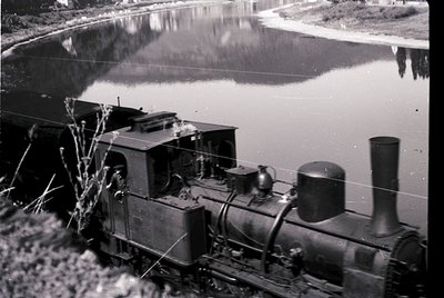 Vintage steam locomotive beside a calm waterway, likely a river or canal, with industrial-era design—noticeable smokestack an...
