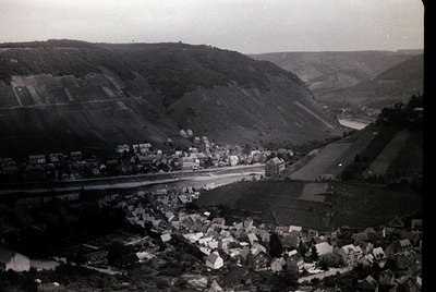 Aerial black-and-white photograph of a rural valley town nestled between rolling hills, likely mid-20th century. Dense cluste...