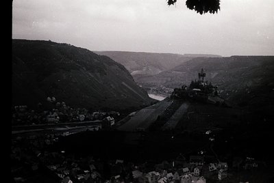 Vintage aerial view of a hilly European town with a prominent castle perched atop a ridge. Agricultural terraces and winding ...