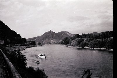 Black-and-white river scene featuring a small motorboat and swimmers in mid-20th century. Prominent hilltop structure resembl...