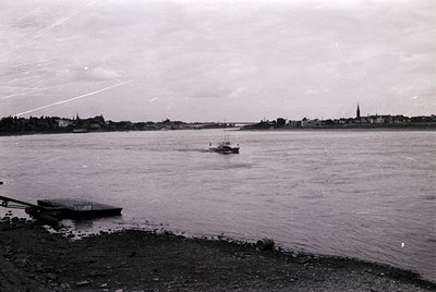 Mid-20th century black-and-white photo of a small ferry crossing a wide river, likely the Elbe or Danube due to urban skyline...
