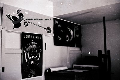 Vintage black-and-white interior featuring mid-century advertising posters. Left: French text ("Nouveau printemps... longue v...
