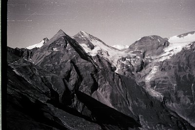 Vintage black-and-white alpine landscape showcasing jagged peaks with patches of snow, likely from the European Alps. Dramati...