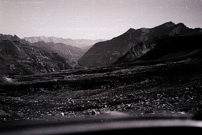 Vintage black-and-white alpine valley scene with jagged peaks and rocky foreground. Mid-20th century film grain and lighting ...