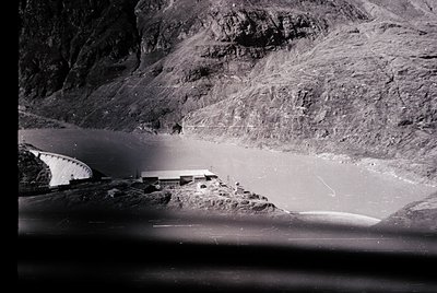 Aerial view of a rugged coastal landscape with steep rocky cliffs and a winding road hugging the shore. Mid-20th century indu...