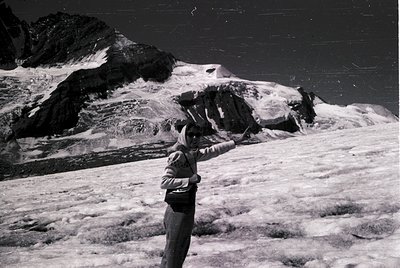 Black-and-white alpine scene featuring a lone climber in mid-ascent, holding a pickaxe. Snow-covered peaks and rugged terrain...