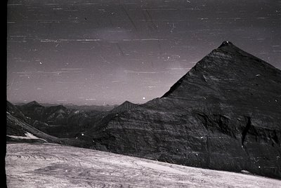 Black-and-white aerial view of the Great Pyramid of Giza, showcasing its iconic triangular silhouette against desert terrain....