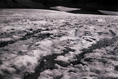 High-contrast aerial view of snow-covered alpine terrain with intricate, winding river patterns beneath. Frosted texture sugg...