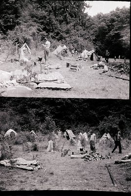 Mid-20th century outdoor camping scene with makeshift shelters and wood-fired stoves. Forest backdrop suggests a rural or wil...