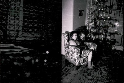 Vintage black-and-white interior shot of a woman in a leopard-print dress seated on a patterned sofa, surrounded by geometric...