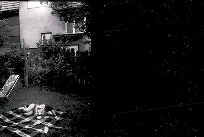 Vintage black-and-white shot of a courtyard scene with a reclining figure on a checkered blanket. Mid-century concrete apartm...