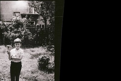 Black-and-white snapshot of a young boy in a backyard, holding a small bird in his gloved hands. Mid-century suburban setting...