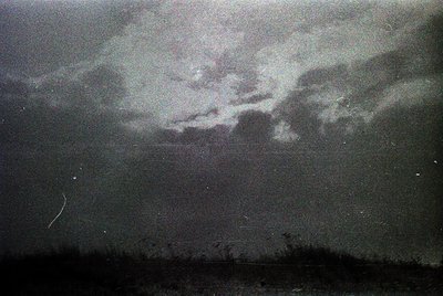 Vintage monochrome photo of dramatic storm clouds over a dark, possibly industrial or urban horizon. Low-light contrast empha...