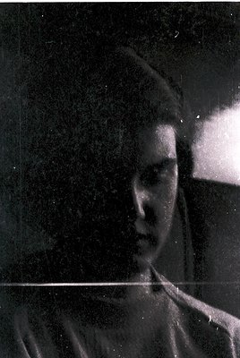 Vintage black-and-white portrait of a young woman in profile, captured through a slightly blurred glass surface. Her hair is ...