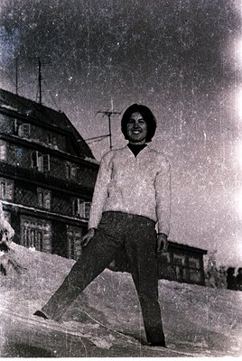 Vintage black-and-white portrait of a person in a short-sleeved sweater and trousers, posing outdoors in snow with a multi-st...