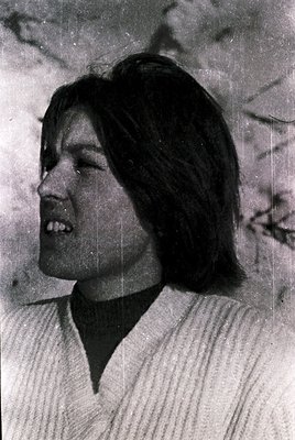 Black-and-white portrait of a person with short, layered hair and a warm smile, wearing a ribbed turtleneck. The vintage film...