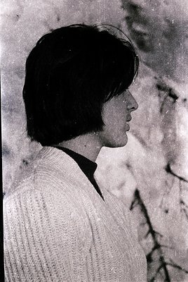 Portrait of a person with short, textured hair and a side profile view, wearing a ribbed sweater. The grainy, monochrome qual...