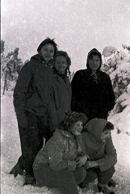 Mid-20th century black-and-white winter portrait: four adults and two children pose on snow-covered ground, bundled in heavy ...