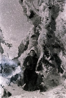 Black-and-white portrait of a woman in alpine terrain, likely mid-20th century. She wears a dark coat, headscarf, and carries...