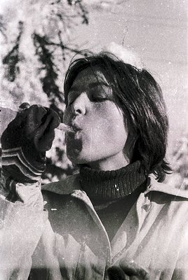 Black-and-white portrait of a person blowing into a handheld device, likely a snow globe or similar toy, outdoors in winter. ...