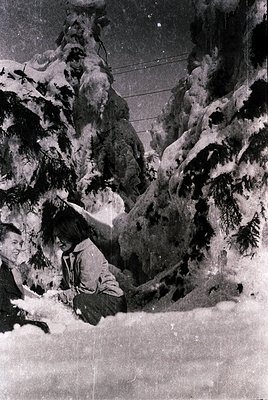 Black-and-white alpine scene featuring a lone figure in mid-ascent on a steep, snow-covered slope. The climber wears a helmet...