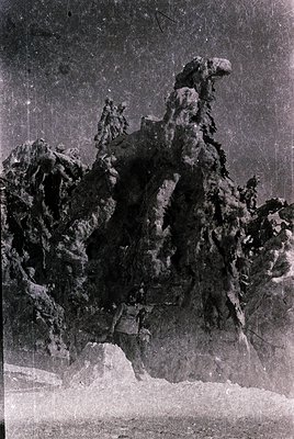 Vintage black-and-white photo of rugged alpine rock formations with jagged peaks and snow patches. The texture suggests weath...