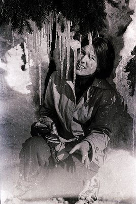 Vintage black-and-white portrait of a person sitting in snow, bundled in a striped winter coat and gloves. Icicles hang from ...