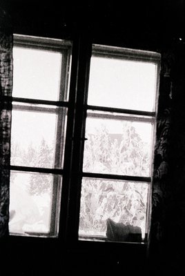Double-pane window framed by aged wood, covered in frost patterns. Interior light contrasts with dark exterior, suggesting wi...