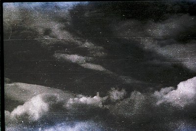 Vintage black-and-white aerial shot of low-hanging clouds over a coastal landscape. Distinctive fog obscures horizon, reveali...