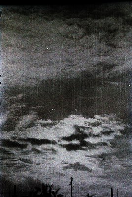Vintage black-and-white photograph of dramatic storm clouds through a slightly aged, textured glass pane. Vertical scratches ...