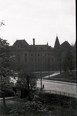 Historic institutional building with Gothic Revival architecture—steeples, arched windows, and symmetrical façade. Overgrown ...