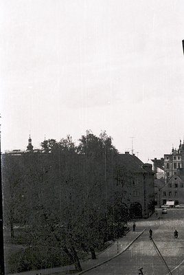 Vintage black-and-white street view featuring early 20th-century European urban architecture. Prominent brick buildings with ...