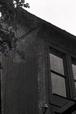 Black-and-white close-up of weathered concrete facade with vertical cracks and exposed aggregate. Single rectangular window f...