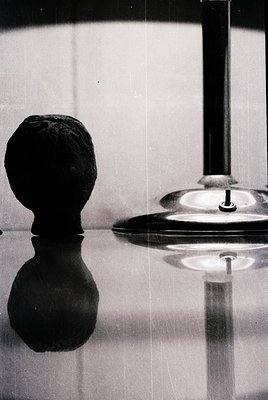 Vintage black-and-white chess piece (king) beside a modernist lamp with reflective base. Minimalist composition highlights co...