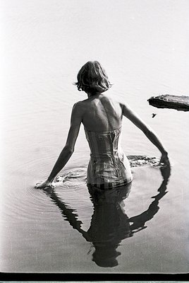 Mid-century swimwear silhouette in shallow water, 1950s–60s beachwear style. Corset-style swimsuit with wide straps and geome...