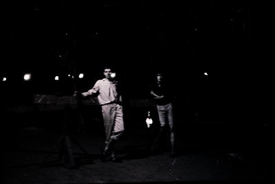 Vintage black-and-white photo of two men in mid-1900s attire—one in a light shirt and trousers, the other in a dark jacket an...