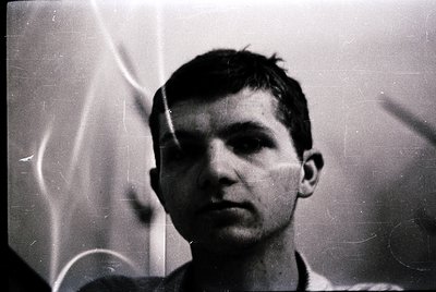Vintage black-and-white portrait of a young man with short, neatly styled hair, shot in low-light. The grainy texture and sli...