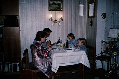 Family dinner scene in a vintage 1970s-style home, featuring warm lighting and classic decor. Three adults and two children s...