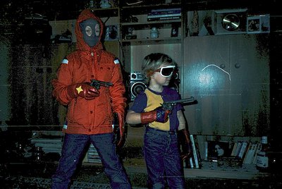Vintage photo of two children in 1970s-style sci-fi costumes—gas masks and futuristic goggles—posing indoors with toy ray gun...
