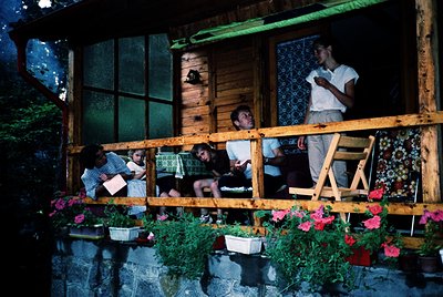 Vintage wooden balcony scene with four adults and a child gathered around a table, illuminated by ambient light. Decor includ...